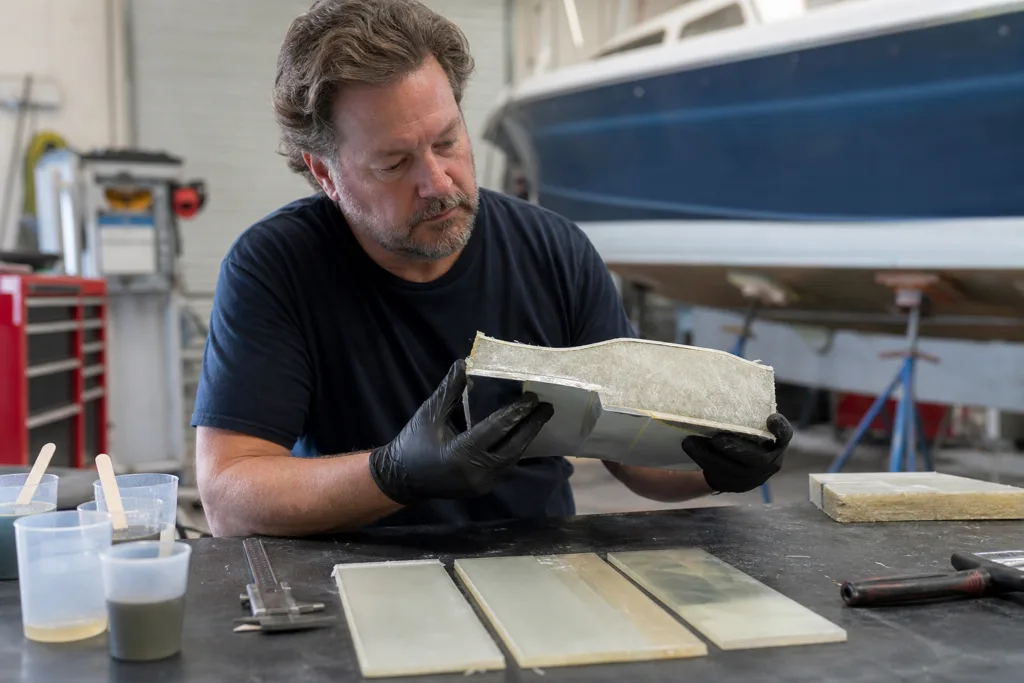 A realistic marine workshop scene showing technical evaluation of laminate samples for resin selection.